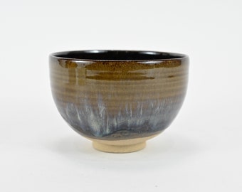 May include: A brown ceramic bowl with a light blue and white glaze. The bowl has a rounded shape and a small foot.