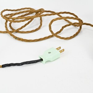 K&ouml;nnte beinhalten: Eine wei&szlig;e Keramik-Tischlampe mit einem braunen Holzsockel und einem gr&uuml;nen Stromkabel mit einem zweipoligen Stecker.