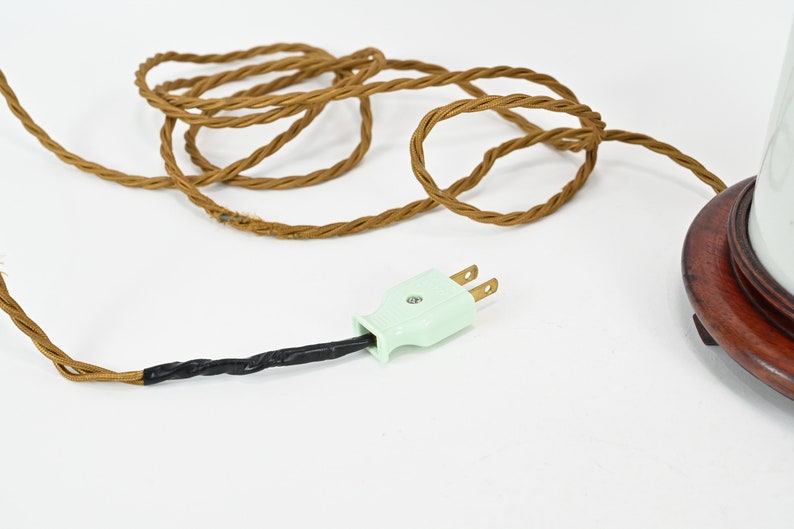 K&ouml;nnte beinhalten: Eine wei&szlig;e Keramik-Tischlampe mit einem braunen Holzsockel und einem gr&uuml;nen Stromkabel mit einem zweipoligen Stecker.