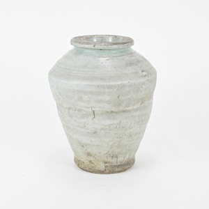 May include: A handmade, off-white ceramic vase with a textured surface and a slightly irregular shape. The vase has a wide body, a narrow neck, and a light blue rim. The base is a darker, earthy tone.