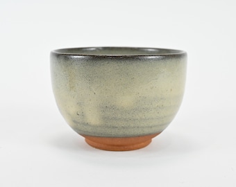May include: A small, round, ceramic bowl with a light green glaze and a brown rim. The bowl has a slightly textured surface.