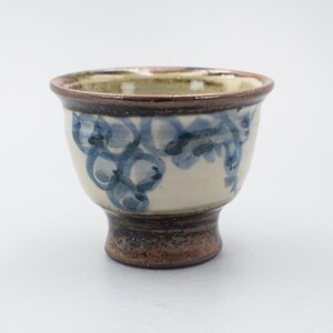 Peut inclure: Une petite tasse en céramique blanche avec un bord et une base bruns. La tasse est décorée d'un motif floral bleu et blanc.
