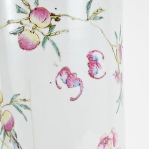 K&ouml;nnte beinhalten: Eine wei&szlig;e Porzellanvase mit floralem Design. Die Vase ist mit rosa und gr&uuml;nen Blumen und Bl&auml;ttern verziert. Die Vase hat eine zylindrische Form und eine glatte Oberfl&auml;che.