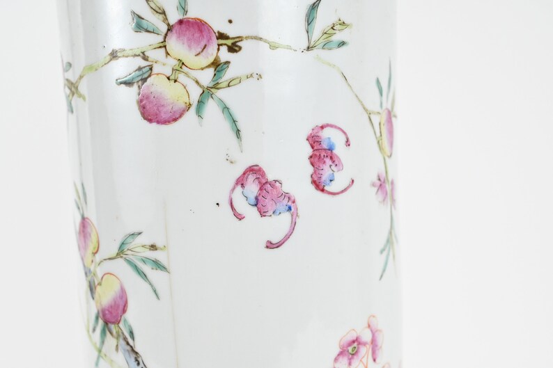 K&ouml;nnte beinhalten: Eine wei&szlig;e Porzellanvase mit floralem Design. Die Vase ist mit rosa und gr&uuml;nen Blumen und Bl&auml;ttern verziert. Die Vase hat eine zylindrische Form und eine glatte Oberfl&auml;che.