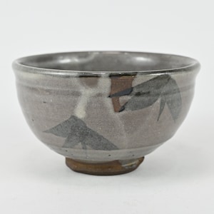 May include: A small, gray ceramic bowl with a brown rim and a design of black and brown leaves. The bowl has a slightly rounded base.