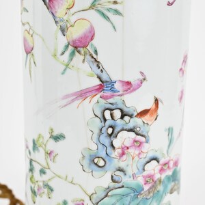K&ouml;nnte beinhalten: Eine wei&szlig;e Porzellan-Lampenbasis mit einem floralen und Vogel-Design. Die Basis zeigt einen rosa und gelben Pfirsichbaum mit einem blauen und rosa Vogel, der auf einem Ast sitzt. Die Basis ist mit gr&uuml;nen Bl&auml;ttern und rosa Bl&uuml;ten verziert.