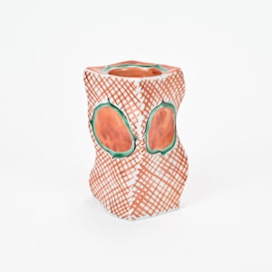 May include: A ceramic vase with a geometric design in shades of orange, green, and white. The vase has a square base and a twisted, cylindrical shape.
