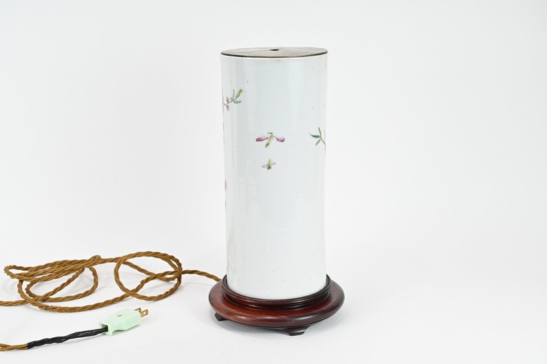 K&ouml;nnte beinhalten: Wei&szlig;e Porzellanlampe mit Blumenmuster und Holzsockel. Die Lampe hat ein braunes Kabel und einen gr&uuml;nen Stecker.