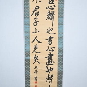 May include: A traditional Japanese calligraphy scroll with black ink on a beige background. The scroll features the text "言心替也書心盡如替尘 形君子小人更笑正本書" which translates to "Words change the heart, and writing changes the heart.  The gentleman and the small person are different, and the book is right."