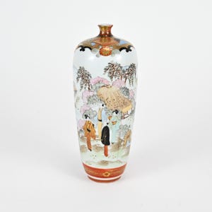 May include: A tall, white ceramic vase with a narrow neck and a wide base. The vase features a painted scene of people and buildings in a landscape, with accents of gold, red, and brown. The vase is a decorative item.