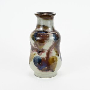 May include: A small, white ceramic vase with a brown, blue, and red glaze. The vase has a rounded body and a narrow neck.