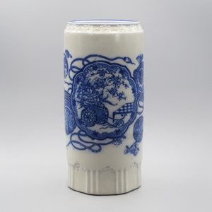 May include: A white ceramic vase with a blue and white floral design. The vase has a cylindrical shape and a scalloped rim.