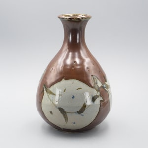 Puede incluir: Un jarrón de cerámica marrón y blanco con cuello estrecho y cuerpo redondeado. El jarrón tiene un diseño floral en marrón y blanco.