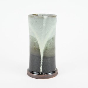 May include: A ceramic vase with a black, green, and white glaze. The vase has a cylindrical shape with a rounded bottom.