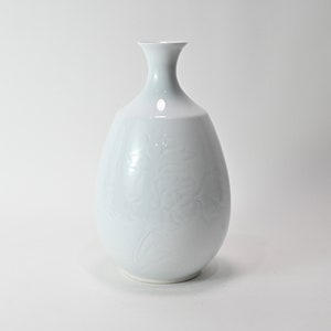 May include: White ceramic vase with a floral design. The vase has a narrow neck and a rounded body.