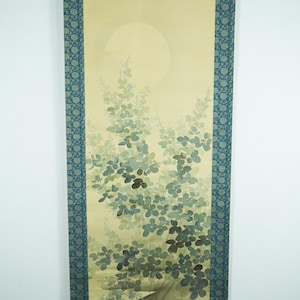 Pode incluir: Pintura em rolo japonesa com uma paisagem serena com uma grande lua pálida e folhagem verde exuberante. A obra de arte é emoldurada por uma borda azul com um padrão floral, criando uma estética tranquila e elegante.