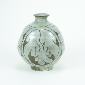 May include: A light blue ceramic vase with a rounded body and a narrow neck. The vase features a dark brown, stylized flame design around the body. The vase is approximately 8 inches tall.