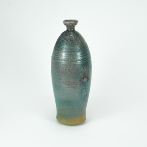 May include: A tall, handcrafted ceramic vase with a textured surface. The vase features a gradient of colors, transitioning from a yellow base to teal and gray tones. The top has a dark gray rim.