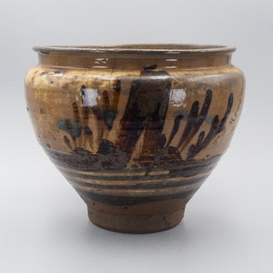 May include: A brown ceramic pot with a wide mouth and a rounded base. The pot is decorated with brown and blue brushstrokes and lines.