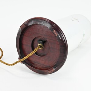 K&ouml;nnte beinhalten: Eine wei&szlig;e Glastischlampe mit einem braunen Holzsockel und einem goldenen Kabel. Die Lampe hat ein schlichtes Design mit einem wei&szlig;en Blumenmuster auf dem Glas.