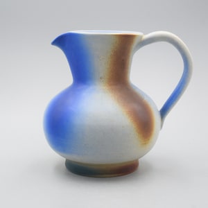 May include: A small, blue and brown ceramic pitcher with a rounded body and a handle. The pitcher has a glazed finish.