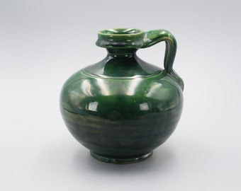 May include: A green ceramic pitcher with a rounded body and a single handle. The pitcher has a glossy finish.