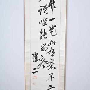 Peut inclure: Un rouleau de calligraphie japonaise traditionnel avec de l'encre noire sur du papier blanc. Le rouleau présente une disposition verticale de caractères chinois, avec un sceau rouge en haut et en bas.