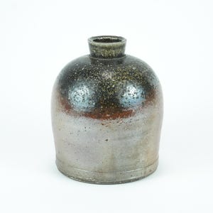Pode incluir: Um vaso de cerâmica artesanal com um corpo arredondado e um pescoço estreito. O vaso apresenta um acabamento metálico salpicado com tons de preto, castanho e cinzento. A forma geral lembra um jarro tradicional.