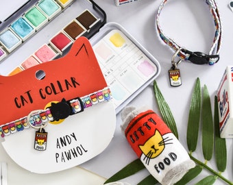 May include: A colourful cat collar with a cat food can charm, a plush cat food can toy, and a watercolour paint set. The collar has the text "CAT COLLAR" and "ANDY PAWHOL" on a red background.