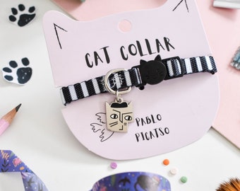 Puede incluir: Un collar para gatos a rayas blancas y negras, con una hebilla negra con forma de gato y un charm plateado con un rostro de gato estilo Picasso. El collar se exhibe en una etiqueta rosa con forma de gato con el texto "CAT COLLAR" y "PABLO PICASSO".