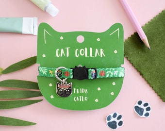 Puede incluir: Collar de gato verde con un dije de gato negro que dice "Frida Catlo". El collar está en una tarjeta verde en forma de gato que dice "Cat Collar".