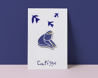 May include: Blue enamel pin depicting a cat with its head tilted back, looking up at four blue birds flying overhead. The pin is displayed on a white card with the text "Catisse" written in blue.
