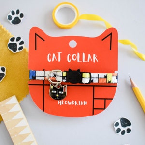 Puede incluir: Un collar de gato rojo con una correa de patr&oacute;n blanco y negro y un amuleto de gato negro. El collar est&aacute; etiquetado como "Cat Collar" y "Meowdrian".