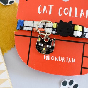 Puede incluir: Una tarjeta roja en forma de gato con el texto "CAT COLLAR" y "MEOWDRIAN". Un collar de gato blanco y negro con un dije de gato negro se muestra en la tarjeta. El dije tiene un acento amarillo y rojo.