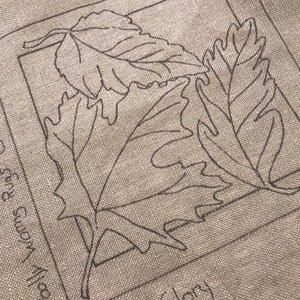 Peut inclure: Un sac fourre-tout en toile beige avec un contour noir de trois feuilles et le texte "Autumn Glory" en écriture noire.