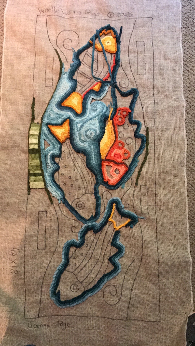 K&ouml;nnte beinhalten: Eine Nahaufnahme eines teilweise fertiggestellten Teppich-H&auml;kelprojekts. Der Teppich ist ein abstraktes Design in Blau, Orange und Gr&uuml;n. Der Teppich ist mit einem schwarzen Rahmen versehen und der Text "Woolly Warms Rugs &copy; 2020" steht in der oberen linken Ecke. Der Text "21 x 44" steht in der unteren linken Ecke und der Text "Joanne Hage" steht in der unteren rechten Ecke.