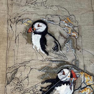 May include: A tan linen fabric panel featuring a partially completed bead embroidery of two puffins. The design includes a hand-drawn outline of a third puffin at the top, with the text "Puffins" and "24 x 48" printed at the bottom.