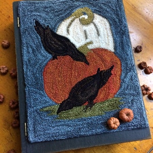 May include: A framed needlepoint artwork depicting two black crows perched on a large orange pumpkin with a white gourd behind it. The background is a dark blue color.