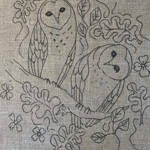 May include: A detailed line drawing of two owls perched on a branch, surrounded by leaves and flowers. The artwork is rendered in dark gray on a textured, light brown background, creating a rustic, natural aesthetic. The owls are the focal point.