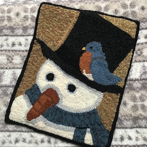 May include: A hand-stitched wool rug depicting a snowman wearing a black top hat and a blue scarf. A bluebird sits on top of the hat. The background is a brown and tan color.