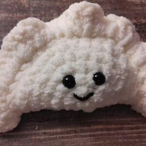 Peut inclure: Un jouet en peluche blanc en crochet en forme de croissant avec un visage souriant et des yeux noirs.