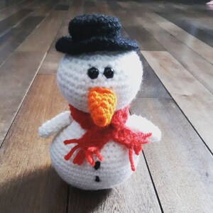 May include: A white crocheted snowman with a black hat, orange carrot nose, and red scarf.
