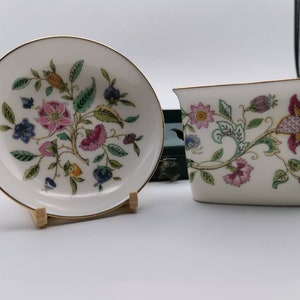 May include: Two white porcelain dishes with a floral design. The dishes are decorated with a pattern of pink, yellow, and green flowers and leaves. The dishes are on a white background.