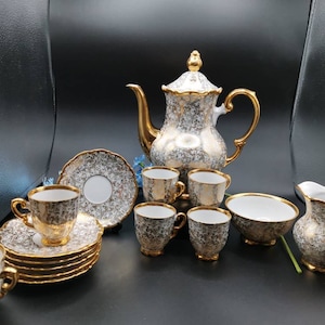 May include: A vintage porcelain tea set with a gold and white floral pattern. The set includes a teapot, creamer, sugar bowl, and six cups and saucers.