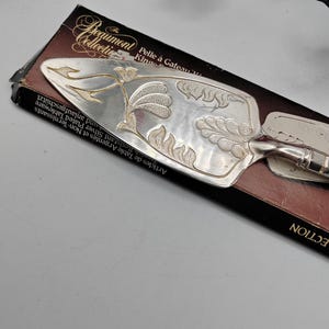 May include: Silver cake server with an ornate floral design. The server is in its original box, which reads "The Beaumont Collective" and "Pelle à Gâteau King".