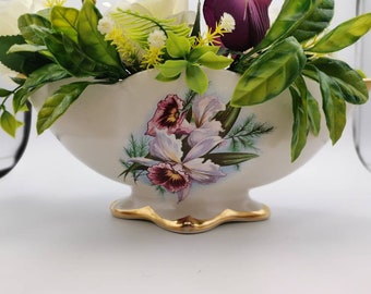 May include: A white ceramic planter with a gold rim and floral design. The planter features a bouquet of white, purple, and green flowers.