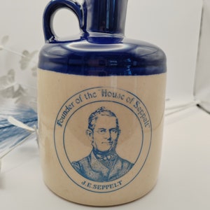 May include: A blue and tan ceramic jug with a handle. The jug has a blue circle with a portrait of a man and the text "Founder of the "House of Seppelt" J.E. Seppelt".