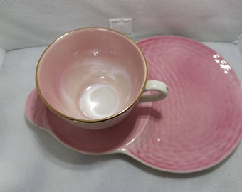 May include: A pink teacup and saucer set with a gold rim. The saucer has a textured design.