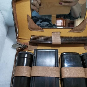 May include: A brown leather travel case with a mirror, a comb, and six black containers with brown leather straps. The case has a zipper closure.