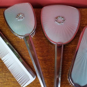 May include: A set of three vintage hairdressing tools, including a comb, a brush with a mirror, and a smaller brush with a mirror. The tools are silver-toned with a white, translucent plastic surface. The mirrors have a decorative design with a silver-toned ring.